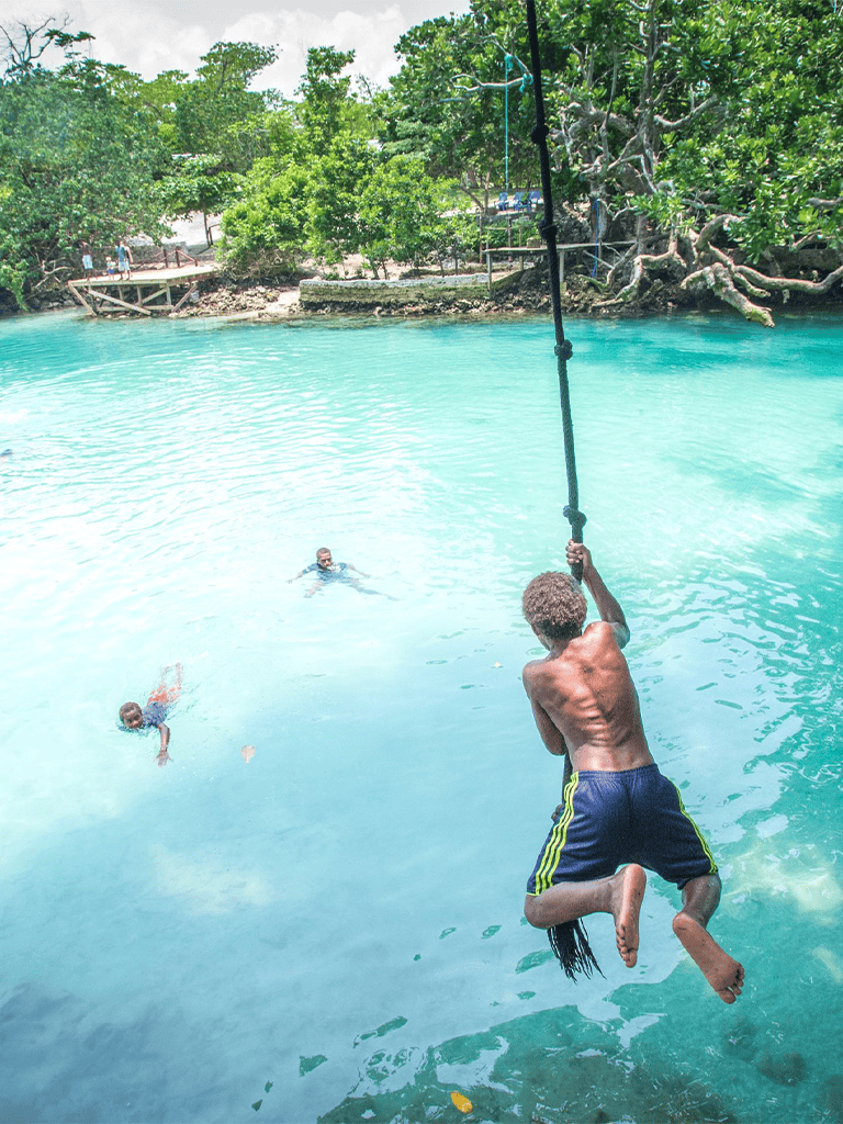 Vibrant tropical water park with kids playing and adults relaxing in lush green surroundings.