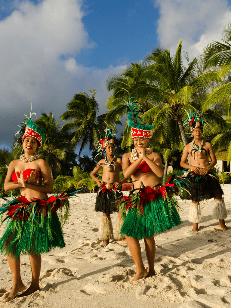 Traditional Polynesian dancers performing on tropical beach with palm trees.