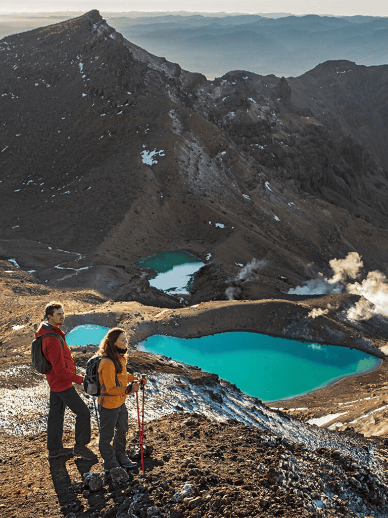 Blue mountain lakes surrounded by rocky terrain and hikers with trekking poles in foreground.