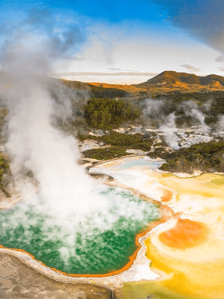 Colorful geothermal hot springs with steam and vibrant mineral deposits in a scenic natural landscape.