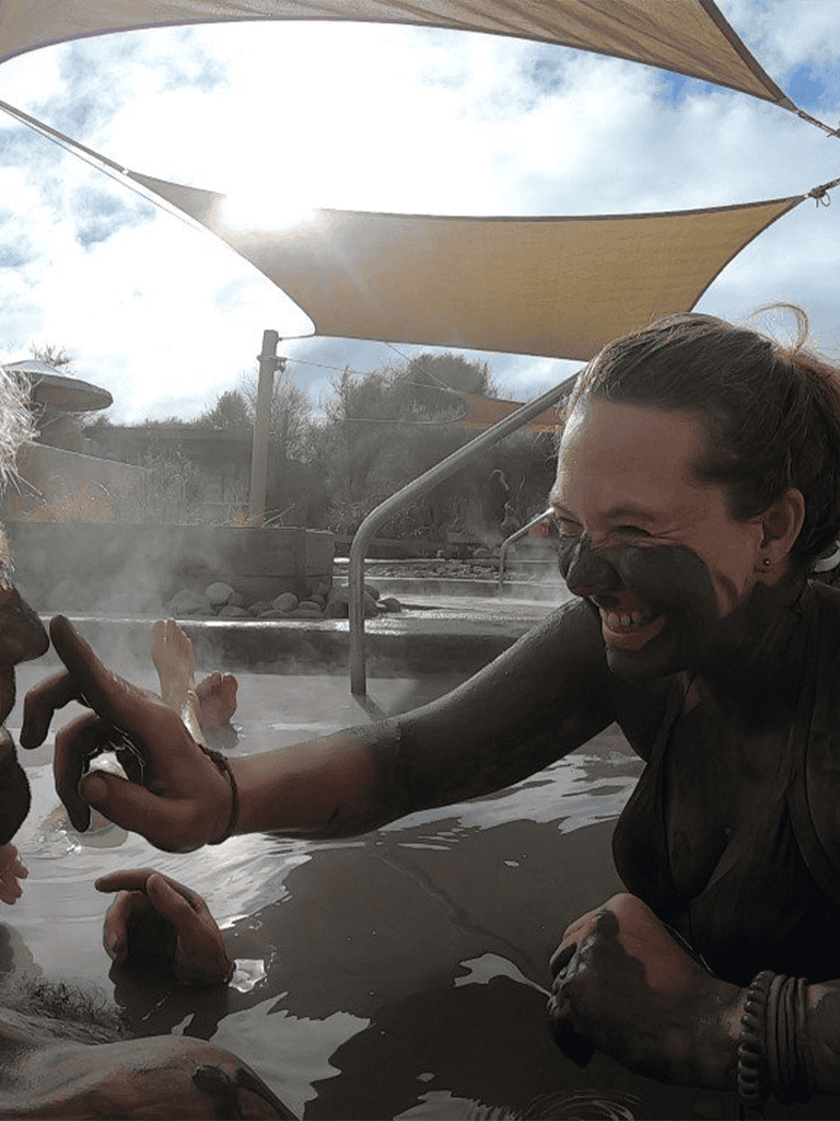 Hot spring therapy in outdoor thermal pool with smiling woman and mud mask, natural relaxation experience.