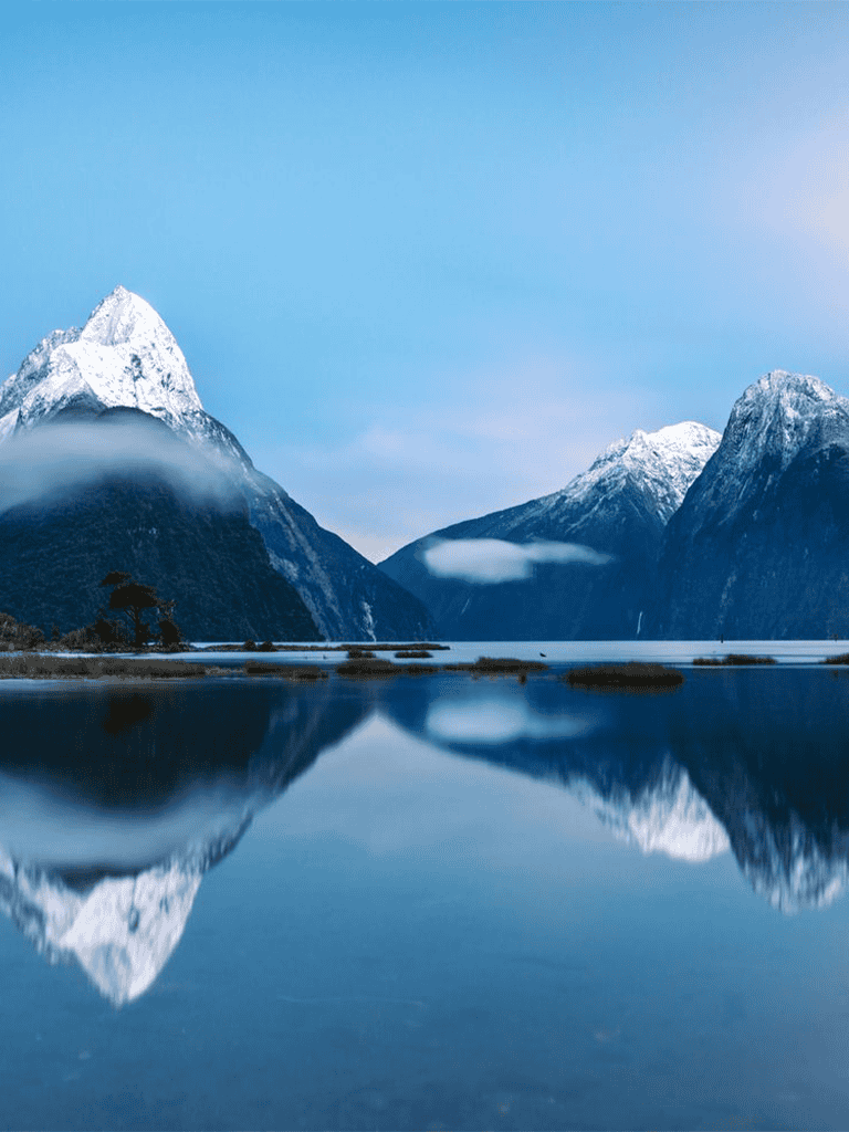 Breathtaking snow-capped mountains reflected in a serene lake under a clear blue sky.