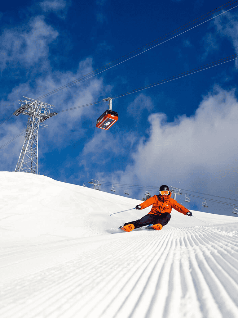 Bright orange skier on groomed snowy slope with ski lift and blue sky at QuestForDirections.