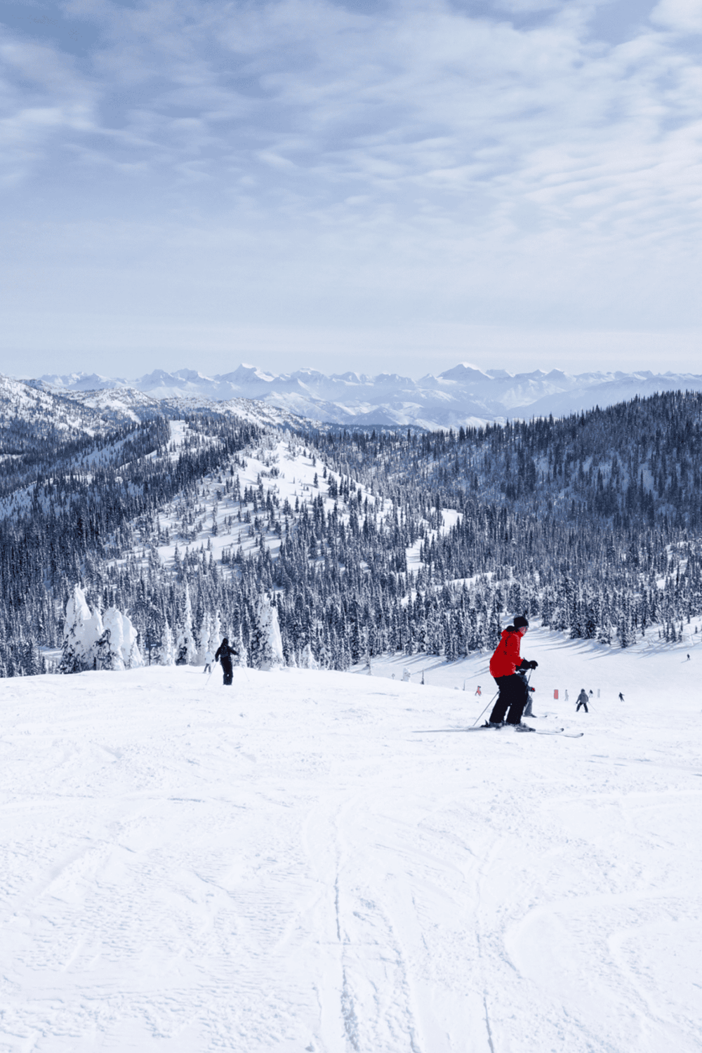 Snow-covered mountain skiing landscape with skier in red jacket, picturesque winter scenery, snow slopes, and forested mountains.