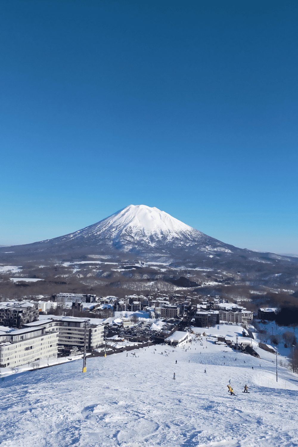 Snow-capped Mt. Fuji view from a ski resort in Japan with skiers on the slopes.