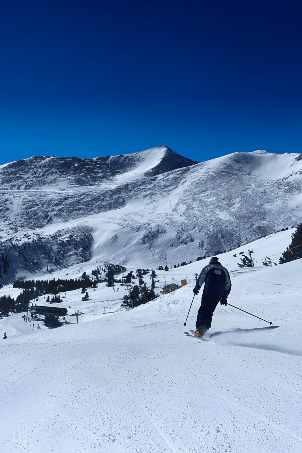 Snowy mountain skier with scenic alpine landscape under clear blue sky.