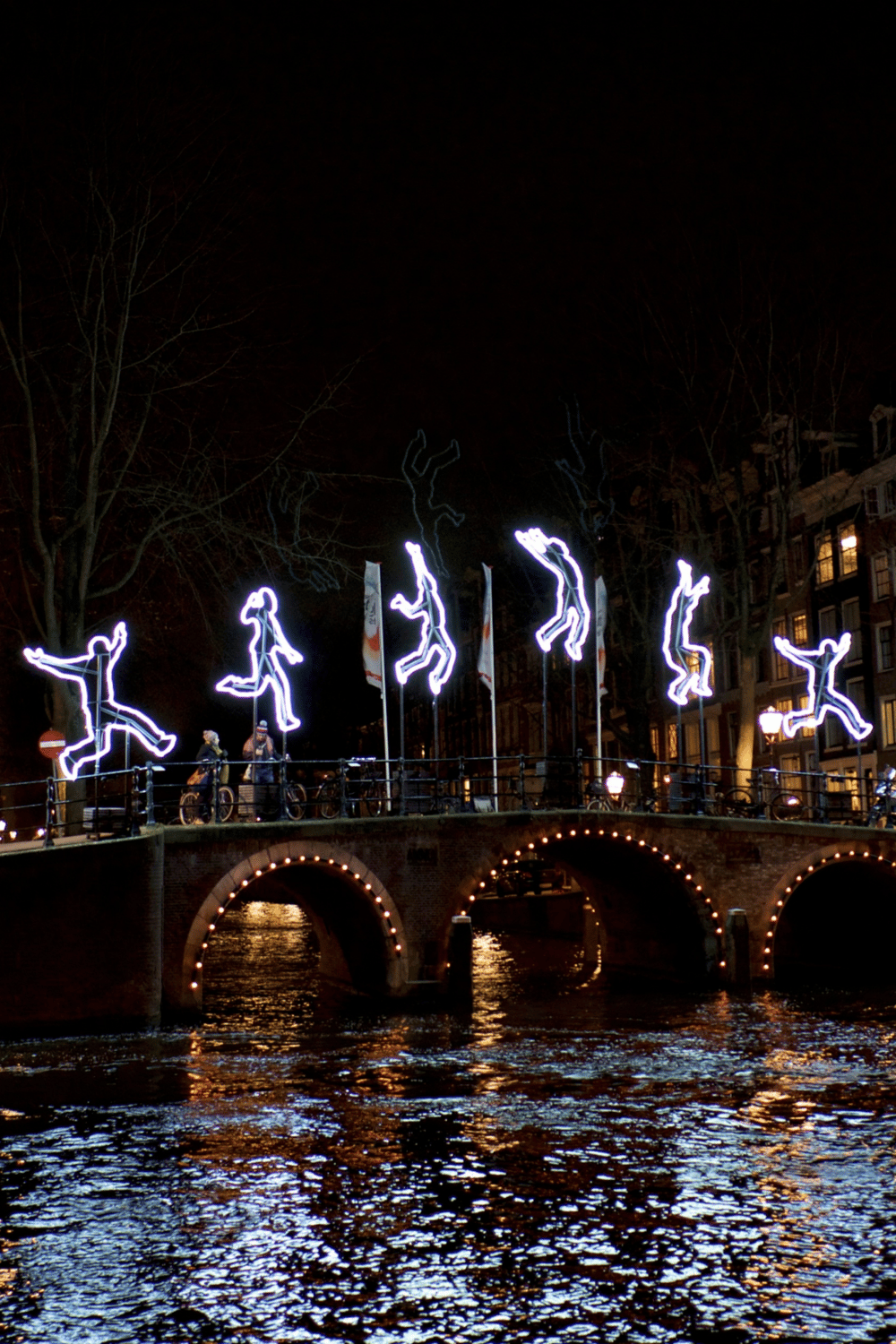 Light art installation on bridge in Amsterdam at night, showcasing digital illuminated dancing figures.
