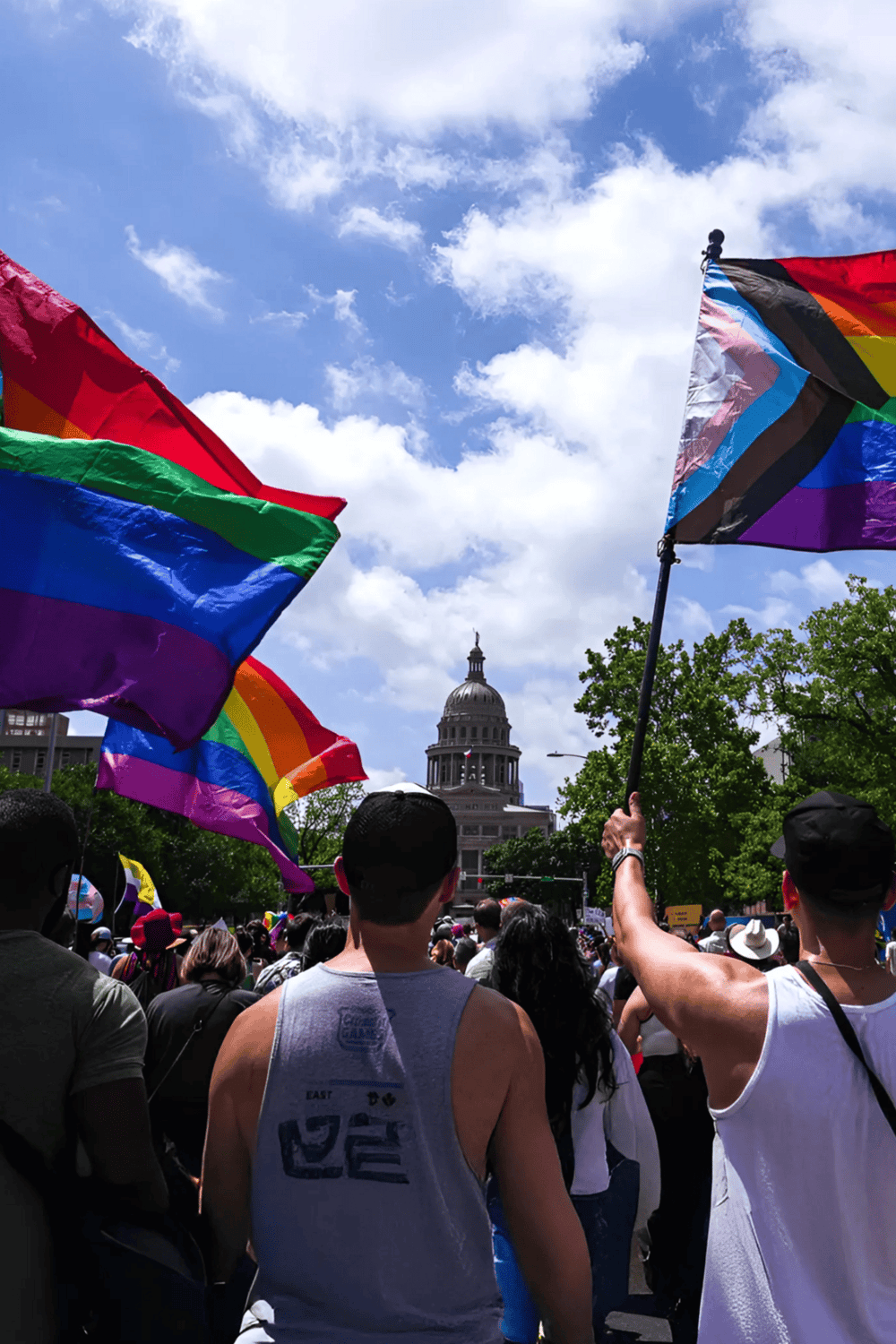 Rainbow flags at a pride parade with the Texas State Capitol in the background.