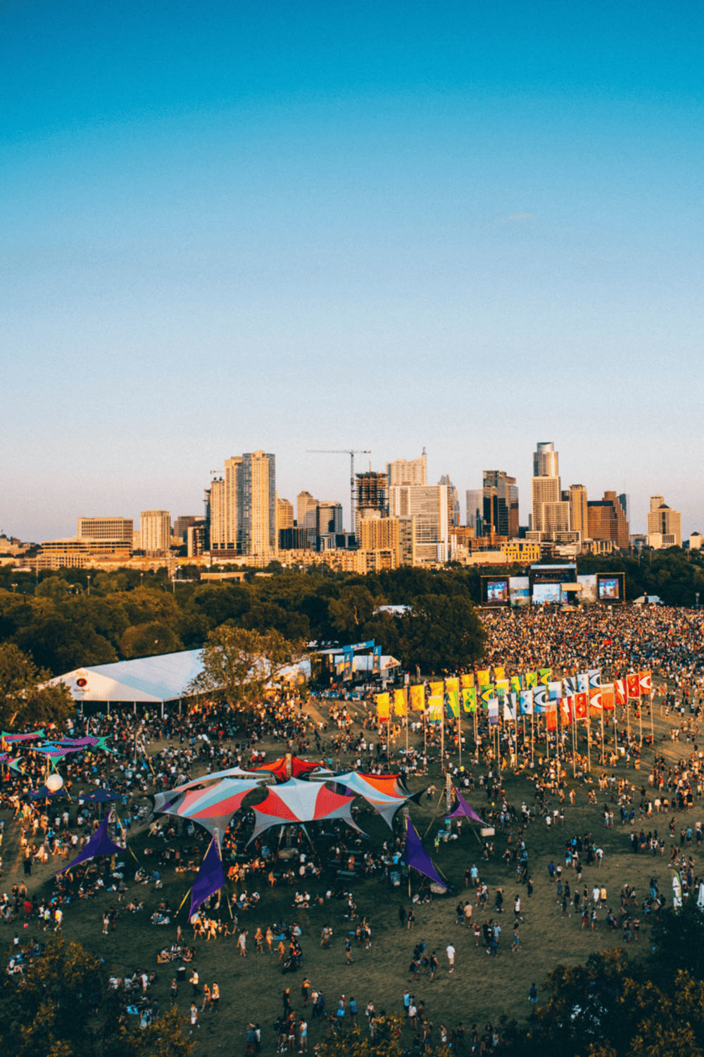 Crowd gathered at outdoor festival with city skyline in the background, lively event in downtown area.