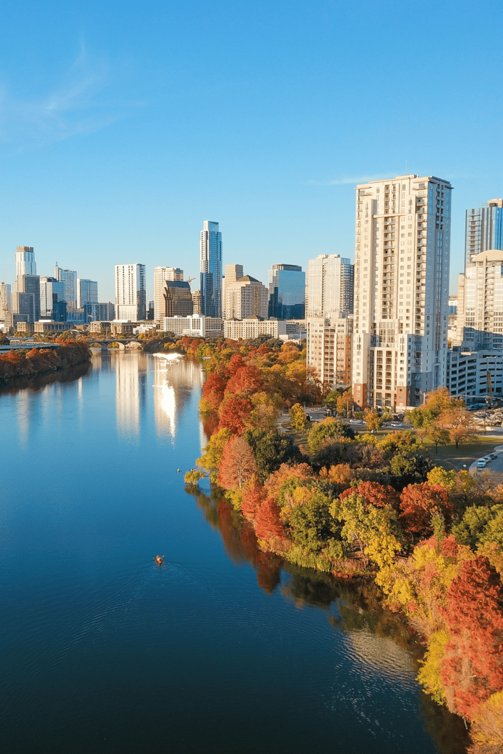 Vibrant autumn cityscape along a river with modern skyscrapers and fall foliage in downtown.