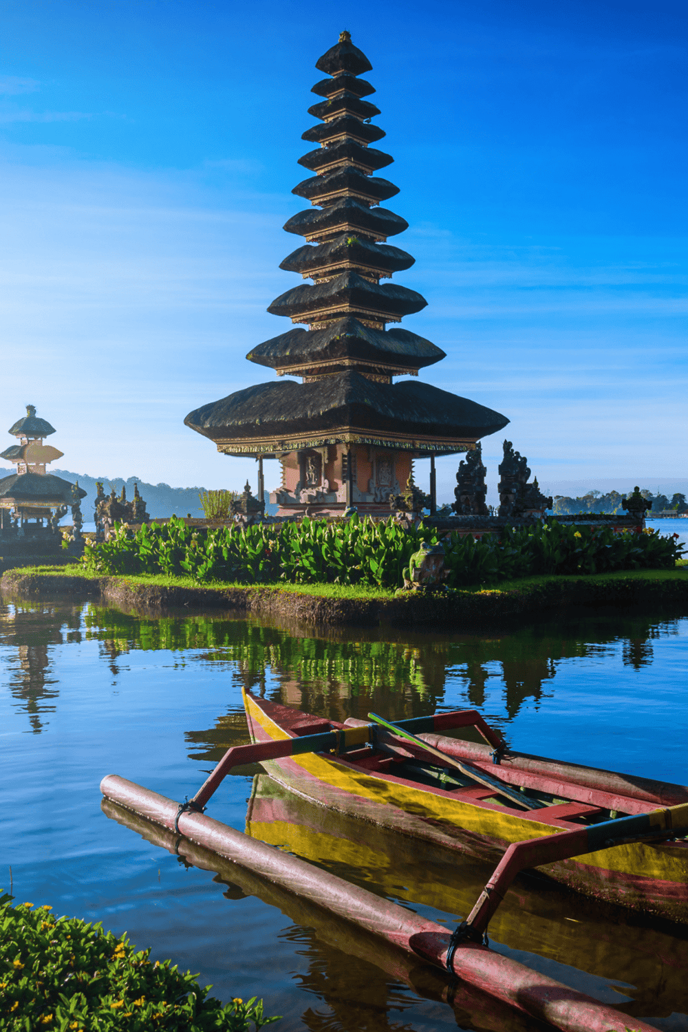 Vintage Balinese pagoda on a lake with traditional boat in Bali, Indonesia.