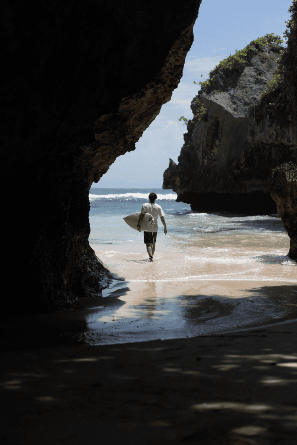 Secluded beach entrance with surfer walking along shoreline and rock formations, scenic ocean view, adventure, travel, and exploration.