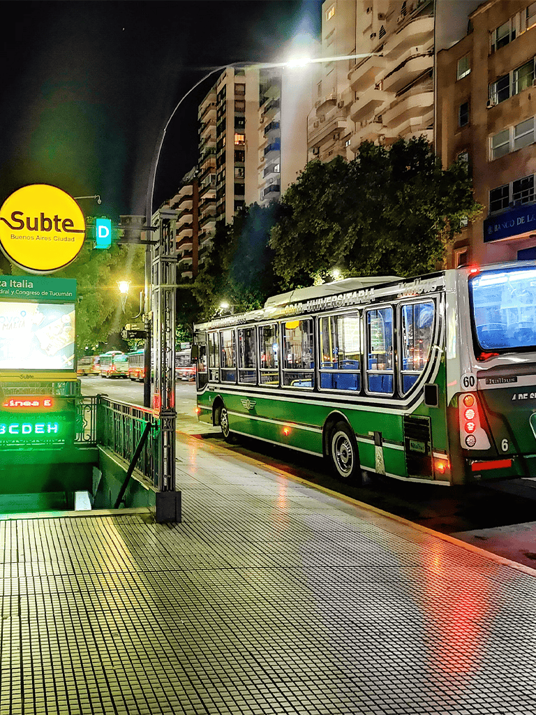 Blue and green bus at Buenos Aires subway entrance at night.