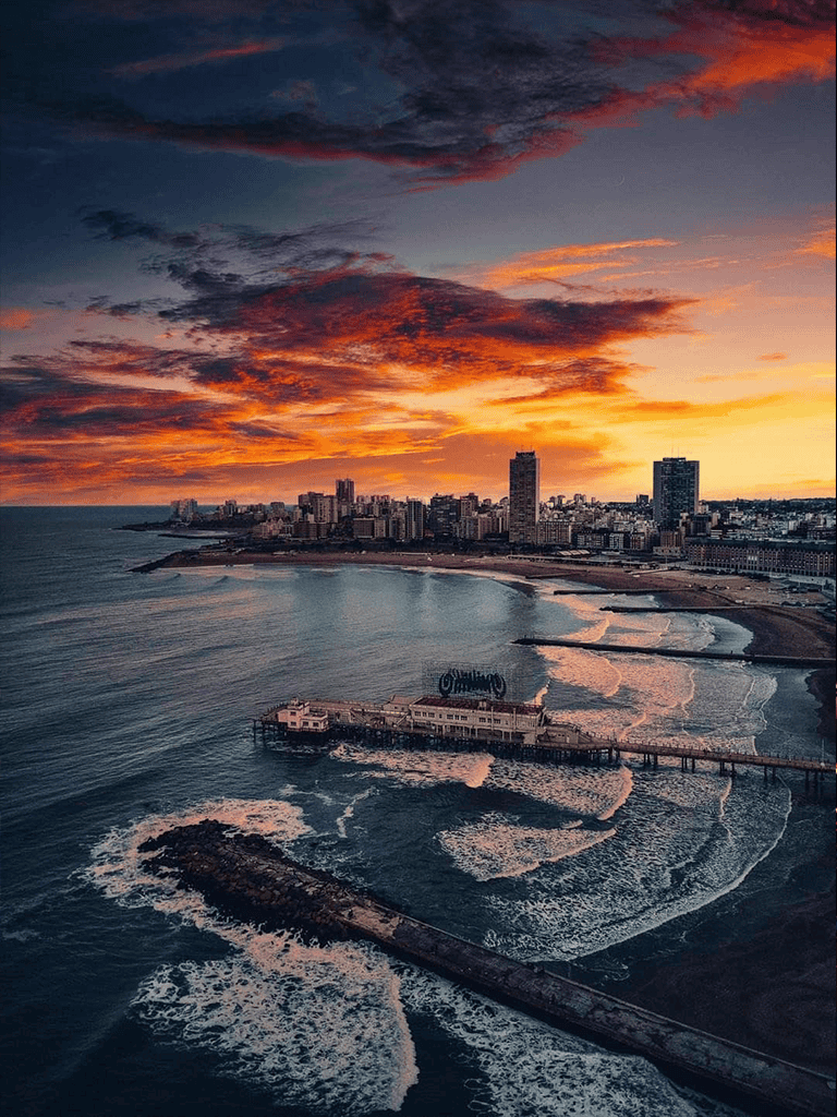 Nighttime coastal cityscape with colorful sunset sky.