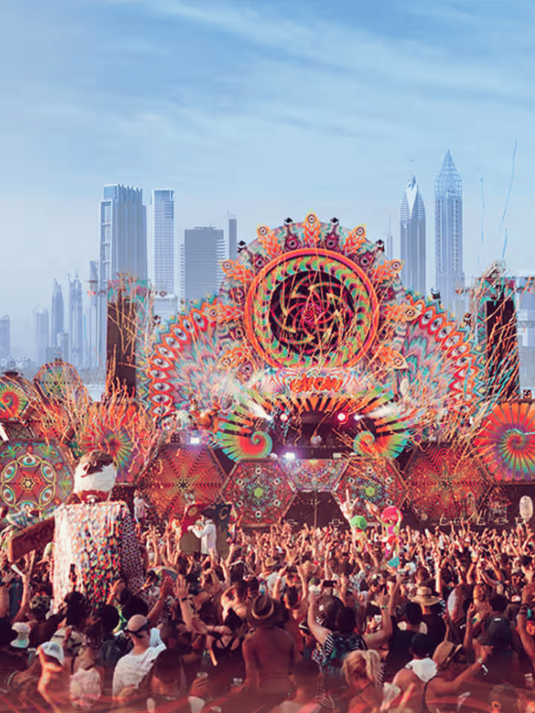 Vibrant electronic music festival with colorful light displays and a large crowd in an urban skyline.