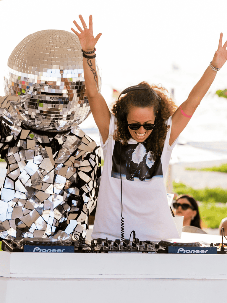 Disco ball costume at a lively outdoor music event with a DJ woman celebrating.