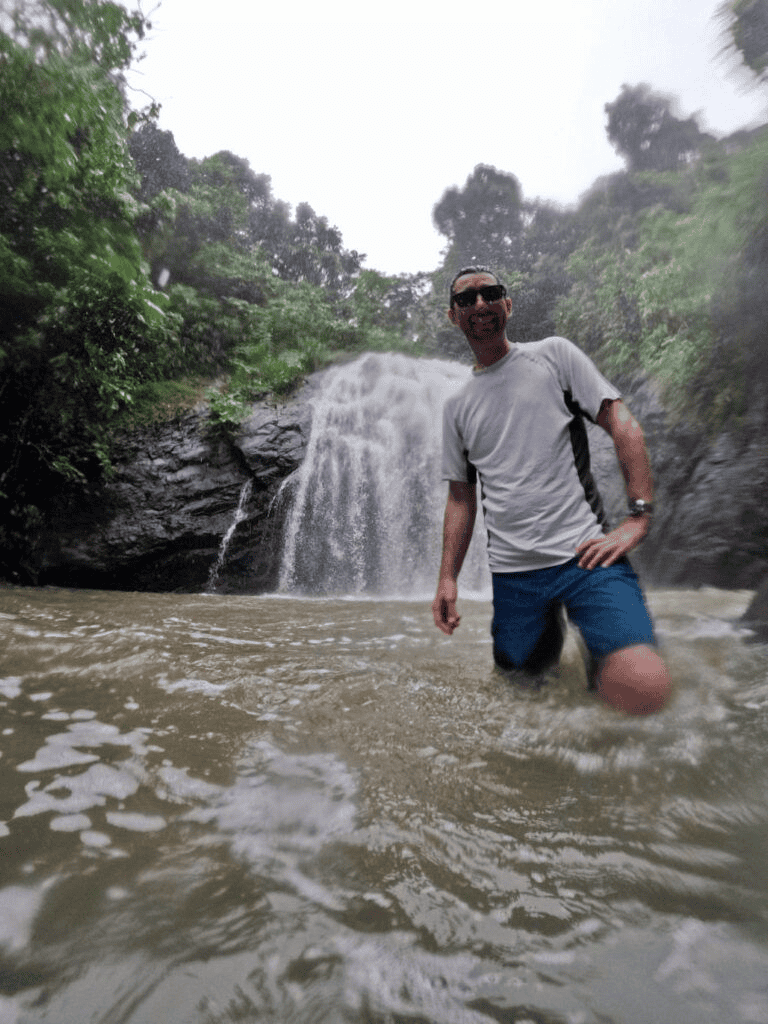 Serene waterfall hike with a man enjoying nature and water adventure in lush green forest setting.