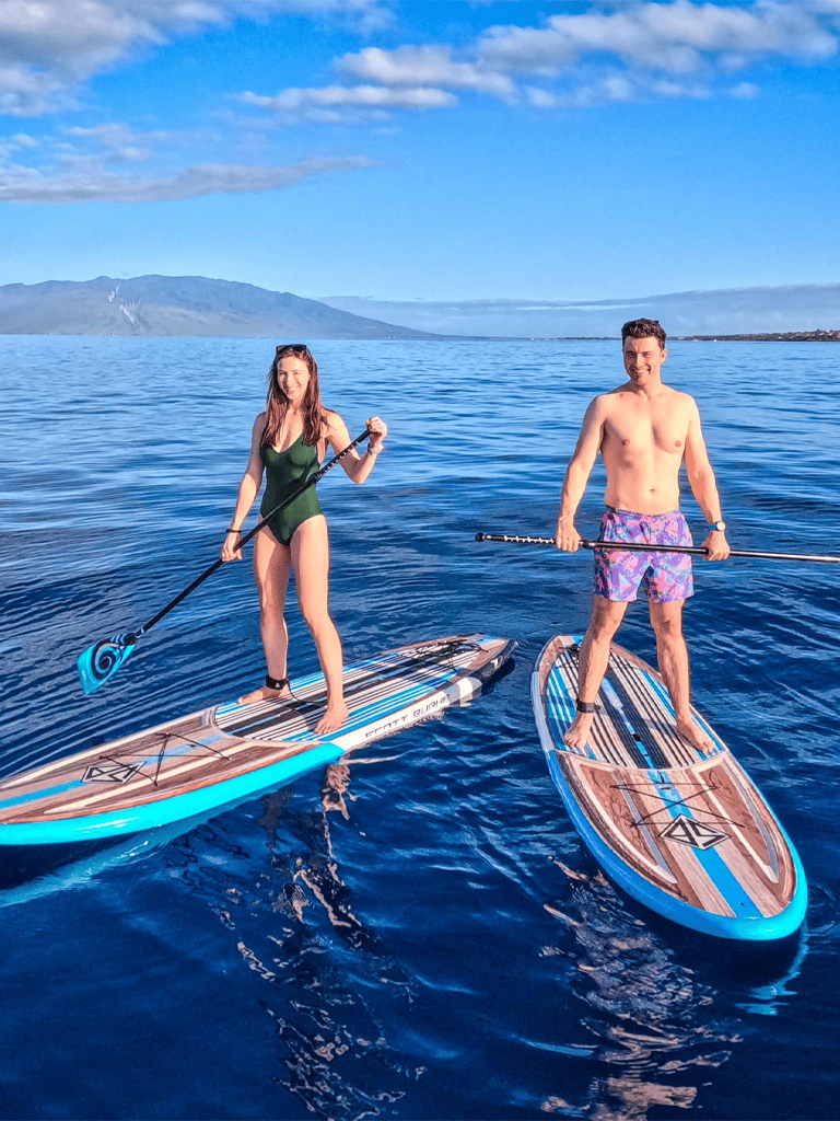 Vibrant stand-up paddleboarding on clear blue water with mountainous background.