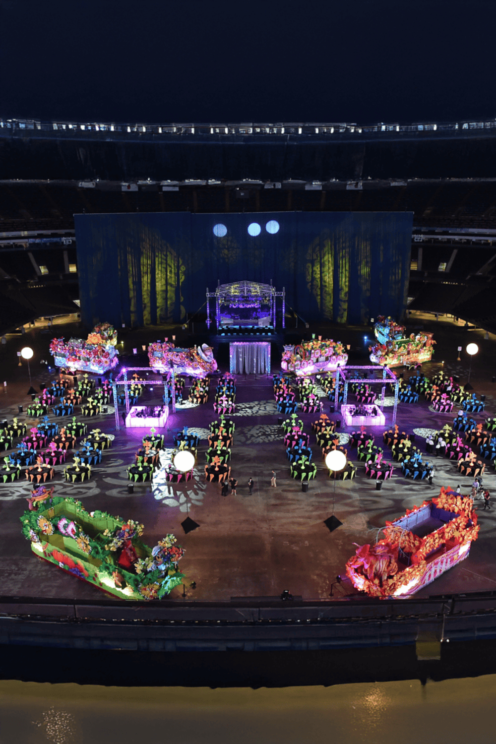 Colorful event setup with floral floats at a stadium during night.