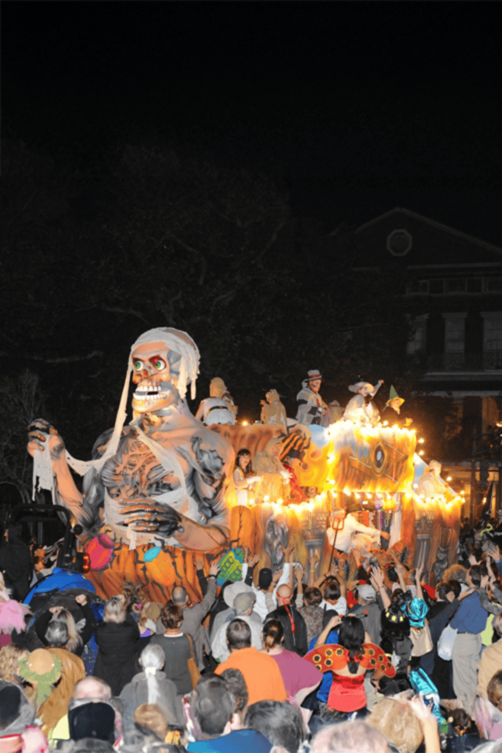 Eerie parade float with skeleton figure during nighttime festival, illuminated and crowd gathered.