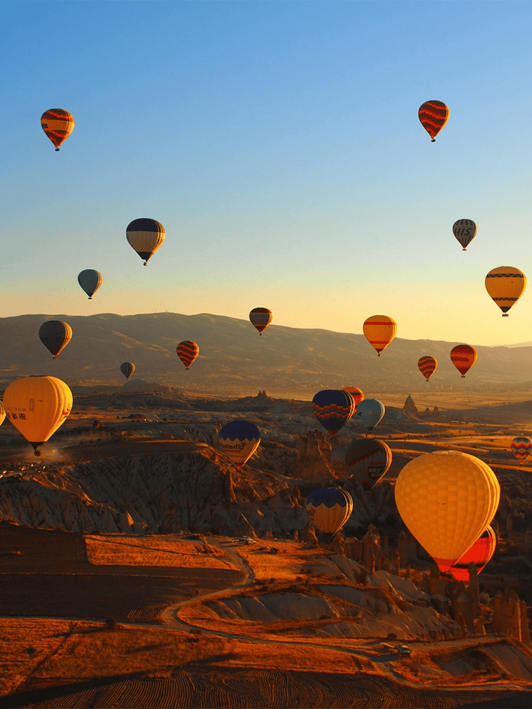 Colorful hot air balloons flying over Cappadocia during sunrise, showcasing travel and adventure.