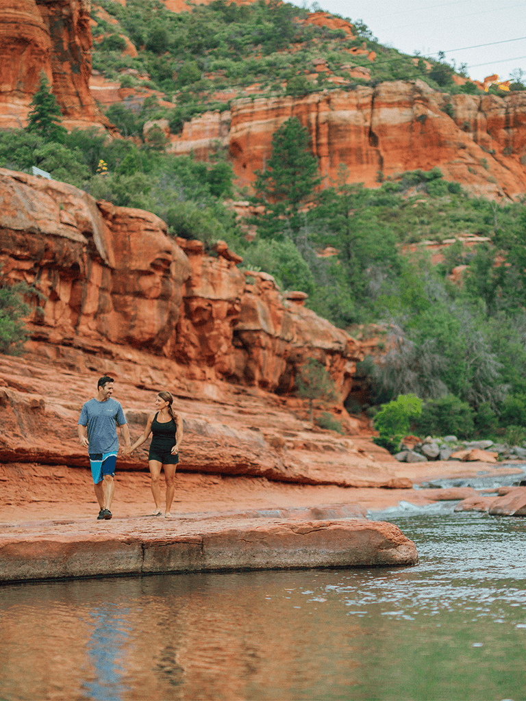 Red rock canyon with hiking couple by the river under clear sky.