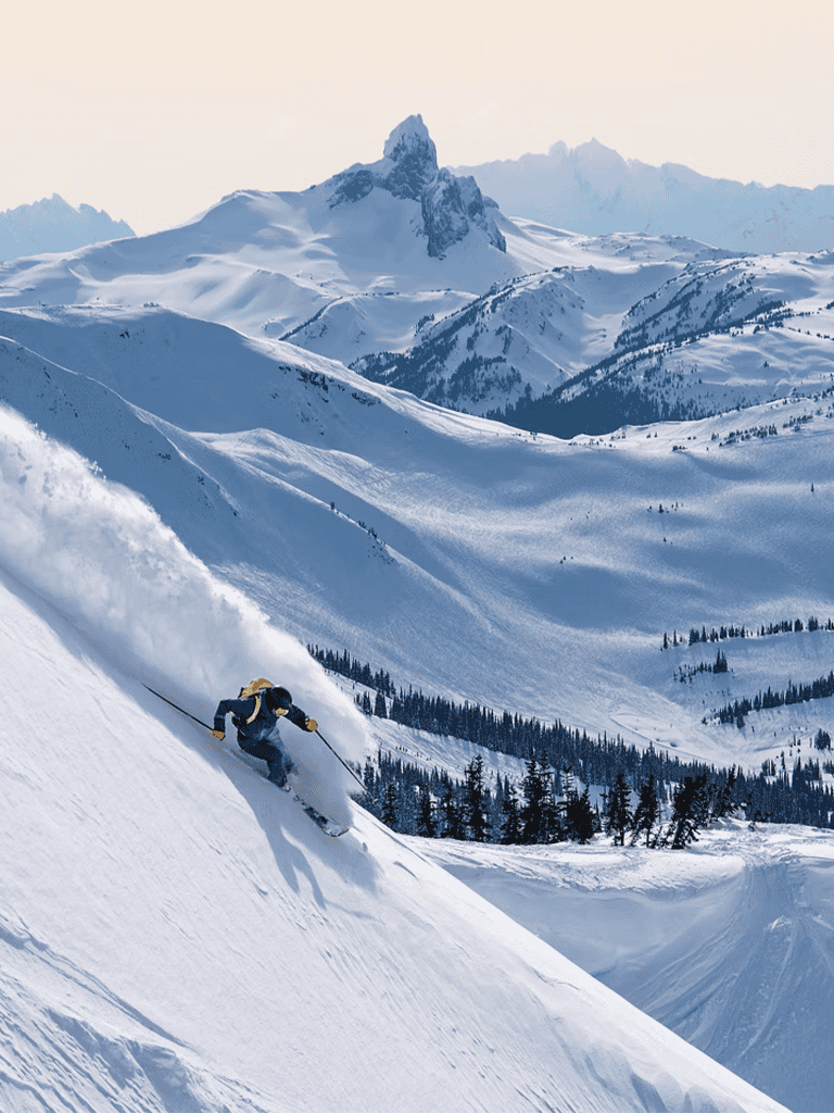 Thrilling skier descending snowy mountain slope with mountainous landscape in background.