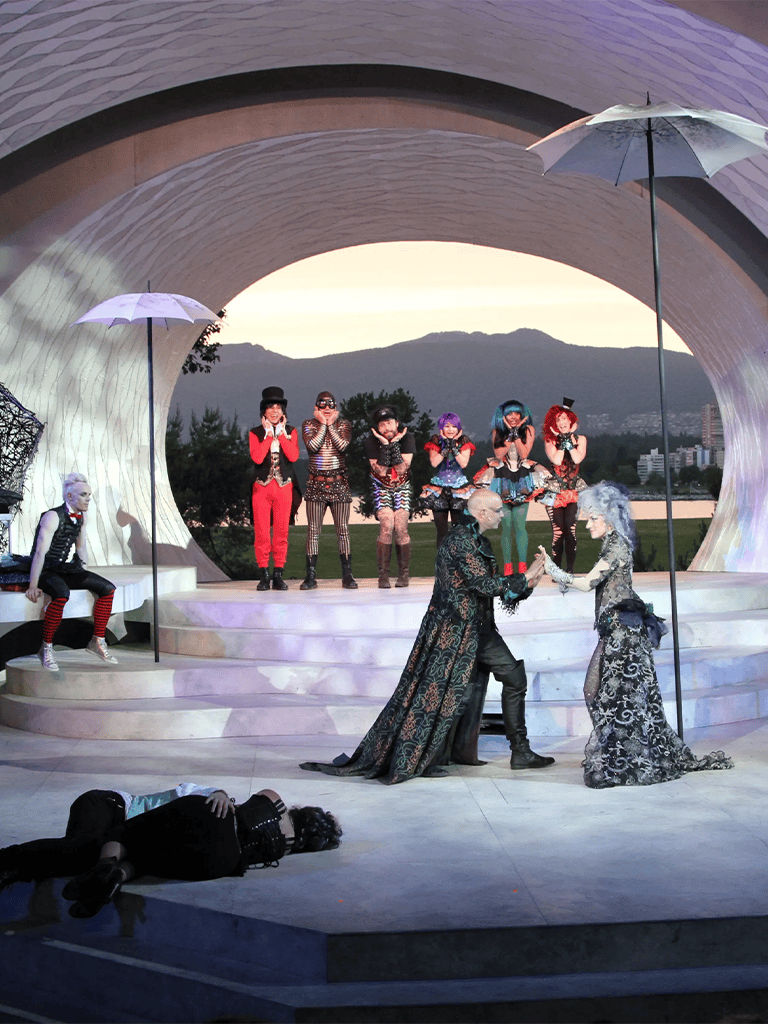 Whimsical theater performance featuring colorful costumes, puppets, and outdoor stage at sunset.