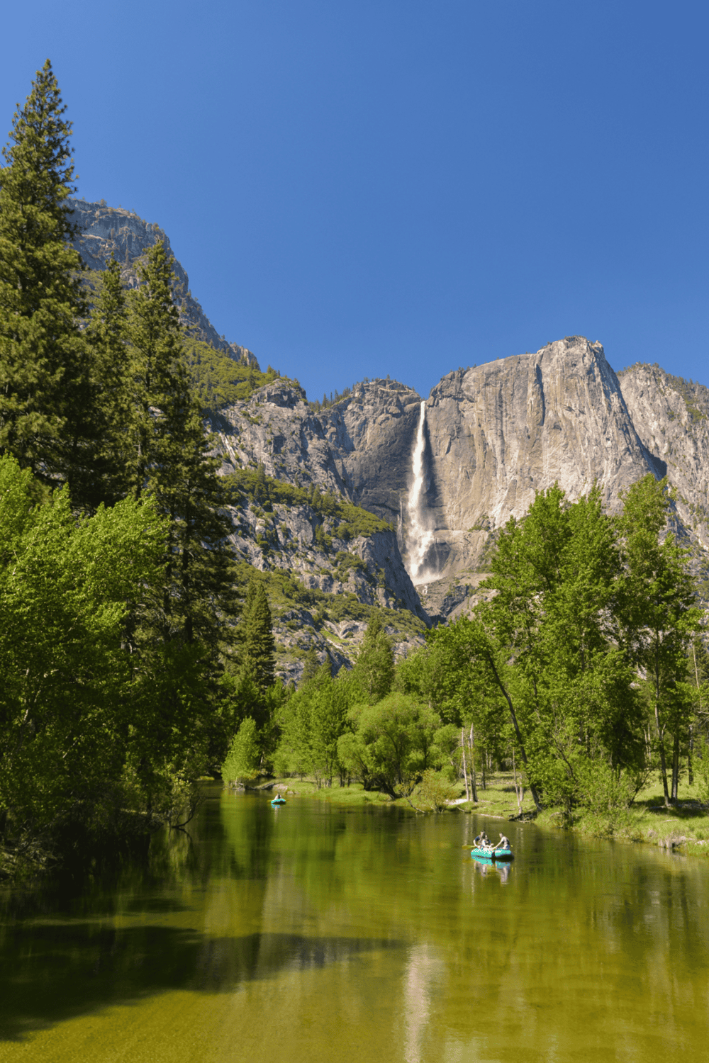 Breathtaking view of Yosemite waterfall with kayakers on the river in lush green forest.