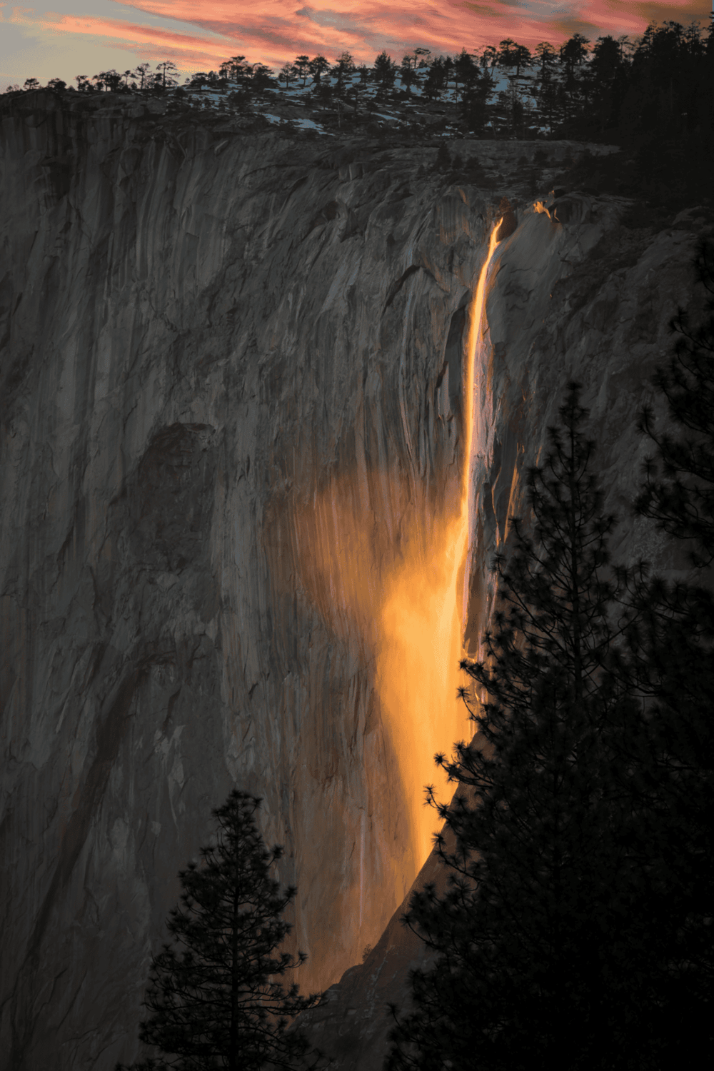 Vernal Fall waterfall at sunset in Yosemite National Park with orange glow and silhouette trees.