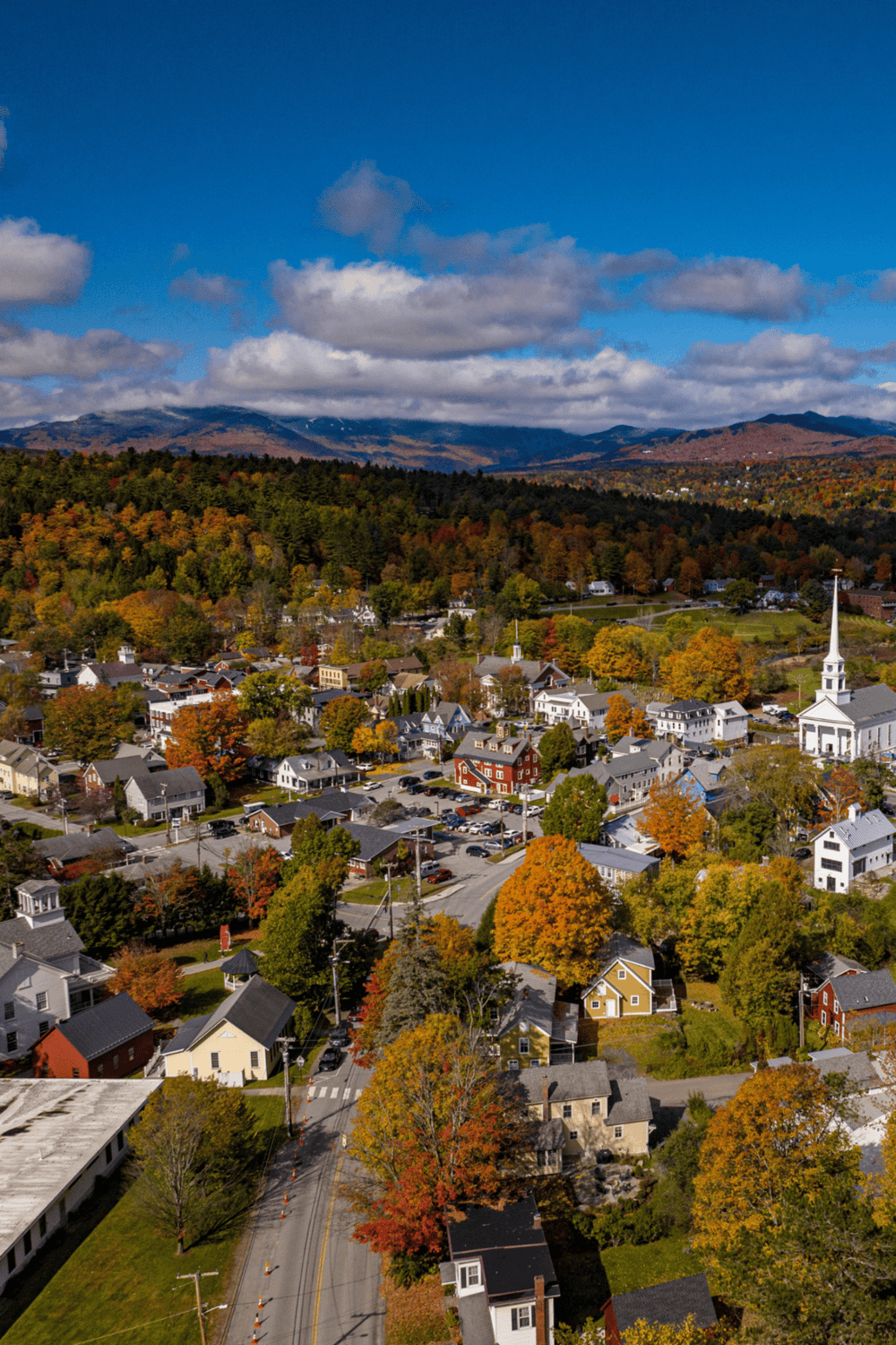 Aerial view of a charming New England town surrounded by colorful fall foliage and mountain scenery.