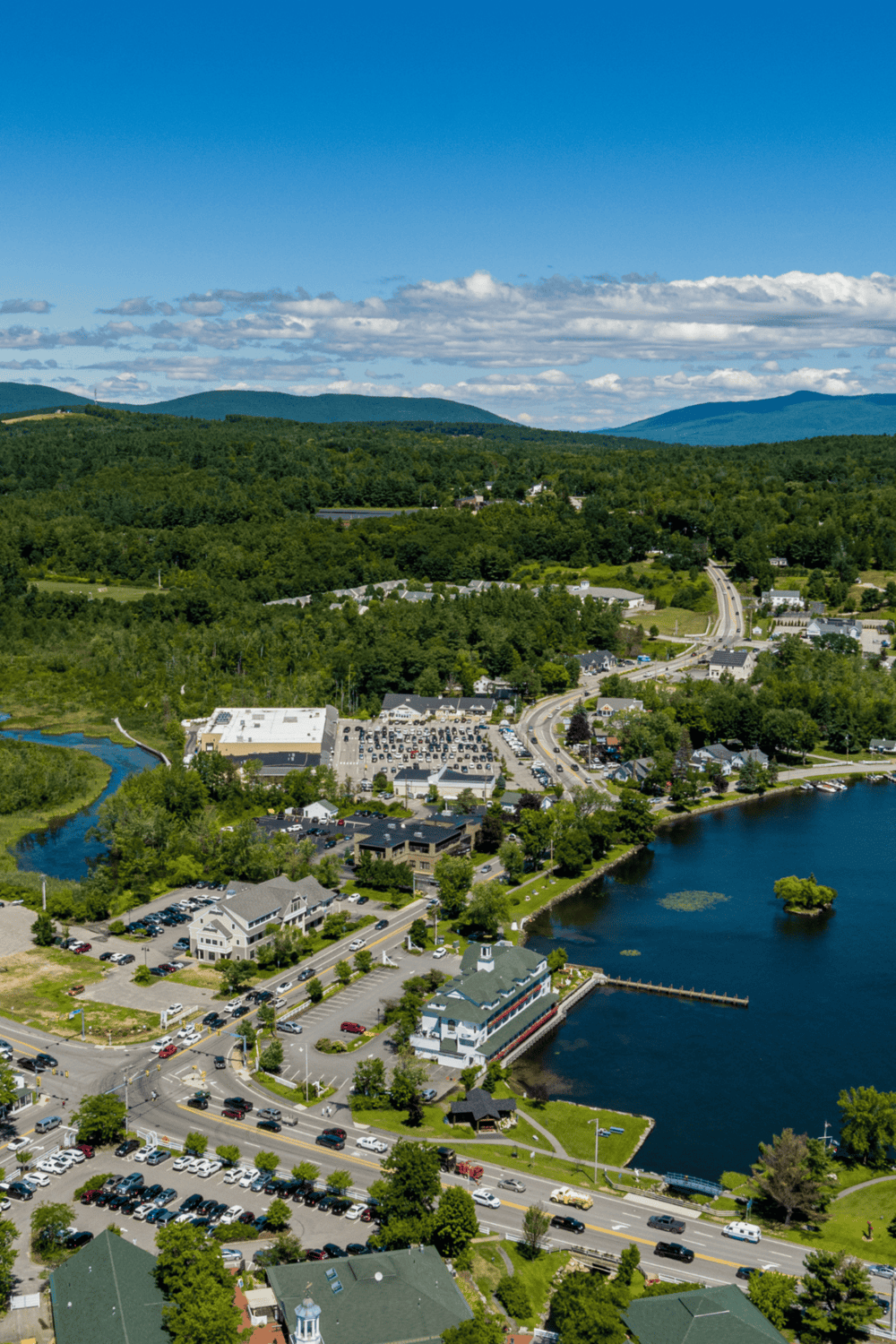 Scenic view of a small town with a harbor, surrounded by lush green mountains and blue sky.