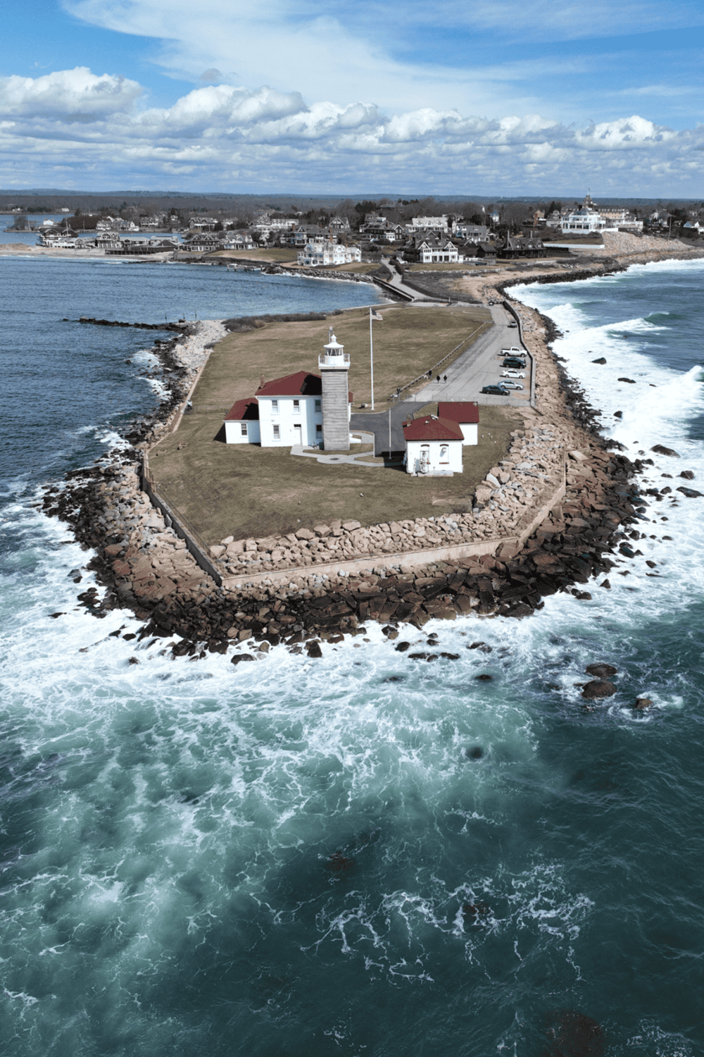 Lighthouse on rocky ocean coastline with scenic seaside town in the background.