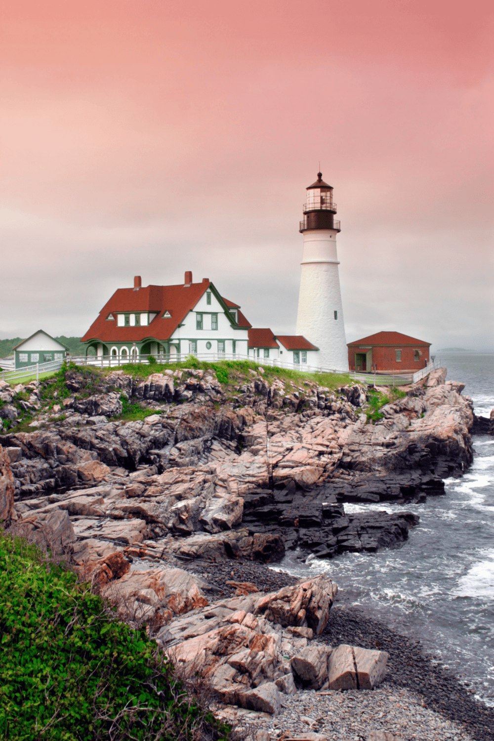 Lighthouse on rocky coast with house, ocean view, sunset sky, coastal scenery, navigation aid, maritime landmark.