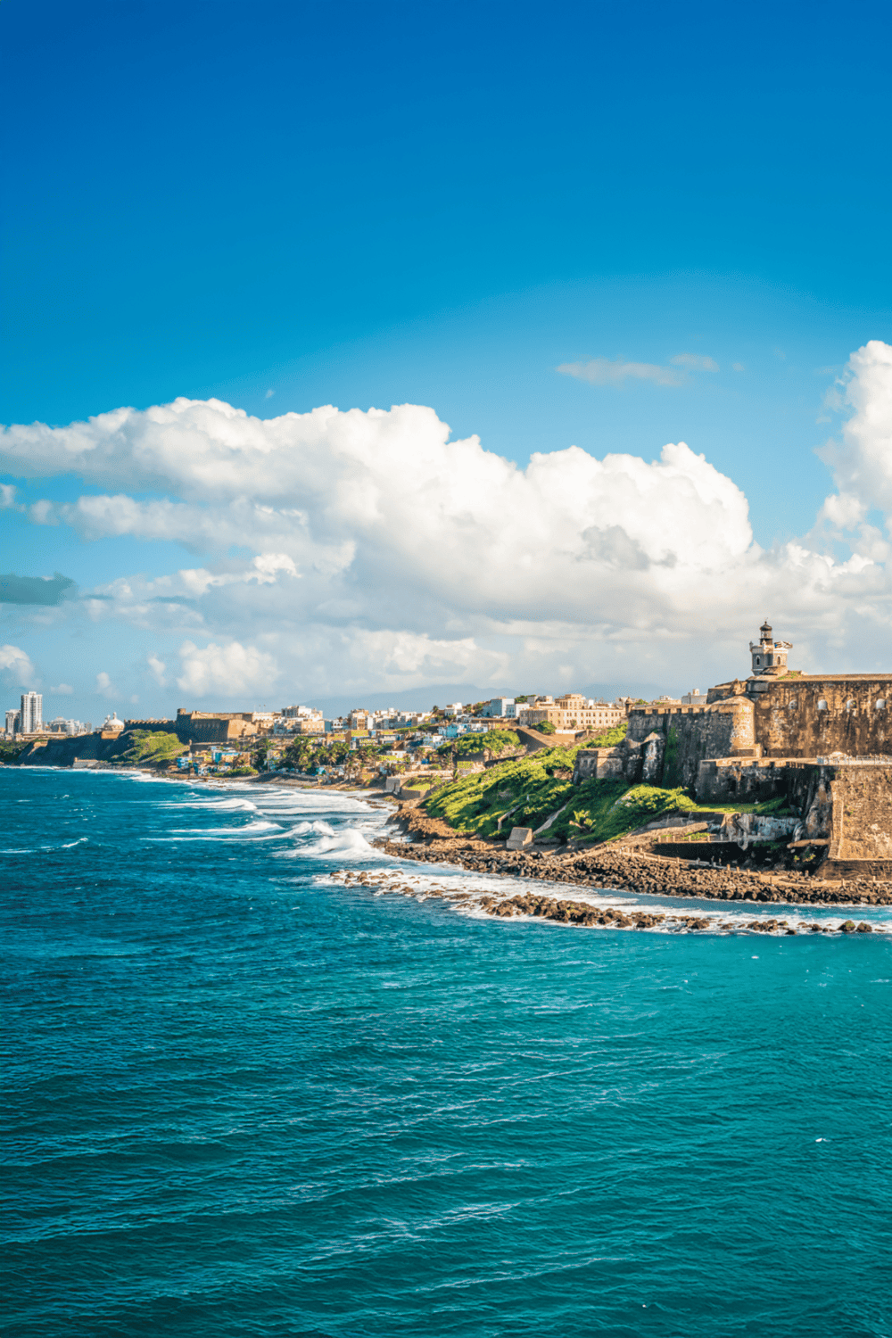 Scenic view of coastal historic fort with city skyline and bright blue sky in the background.