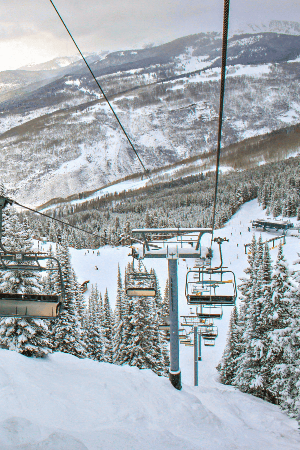 Snowy ski lift with mountain and forest scenery, winter outdoor adventure, mountain ski resort, snow-covered landscape.