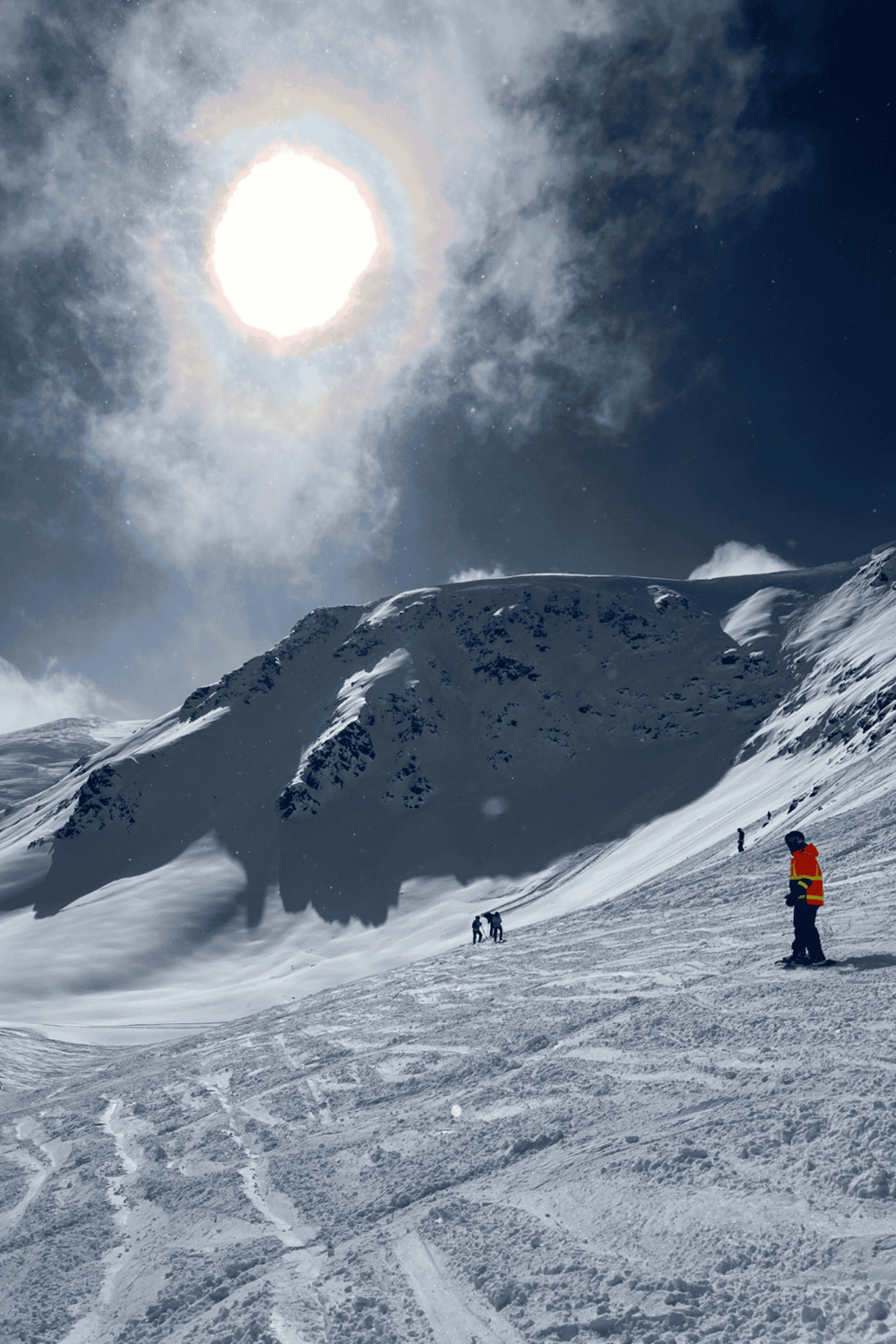 Bright snowy mountain landscape with skiers under a luminous sun and dramatic sky, perfect for adventure travel SEO.