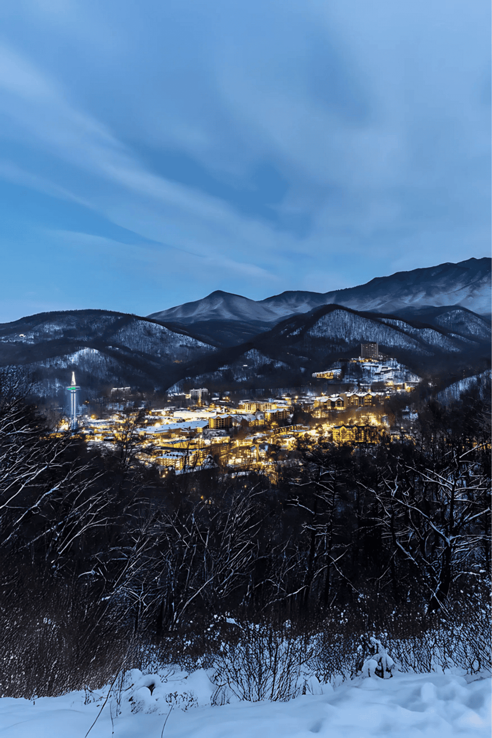 Snowy mountain town illuminated at night with city lights visible, scenic winter landscape for travel planning.