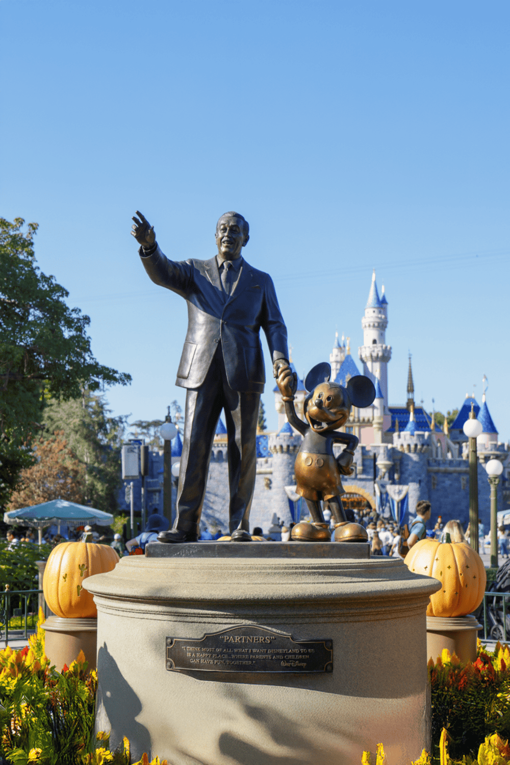 Bronze statue of Walt Disney and Mickey Mouse at Disneyland with Sleeping Beauty Castle in background.