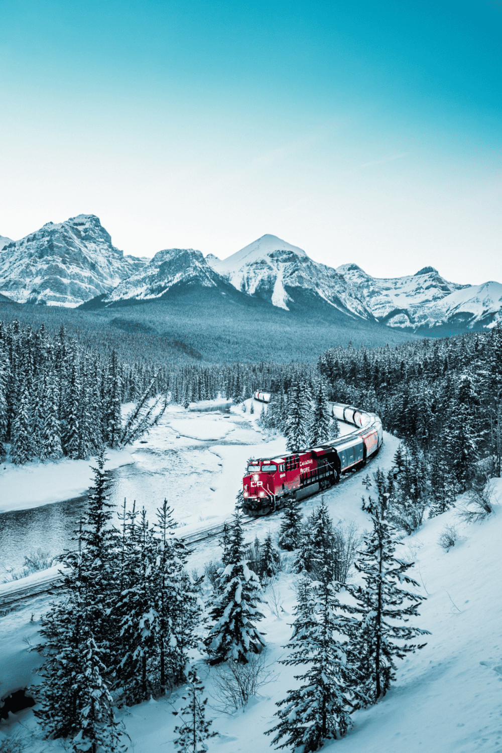 A snow-covered mountain landscape with a red train traveling through a forested winter scene.