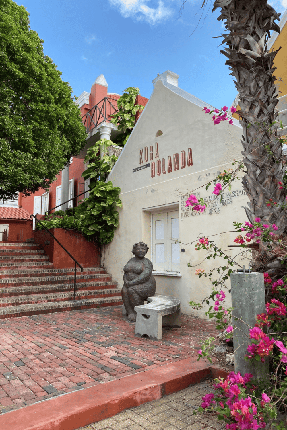 Colorful historic building with "Kura Hulanda" sign in Curaçao, vibrant architecture, and lush plants.