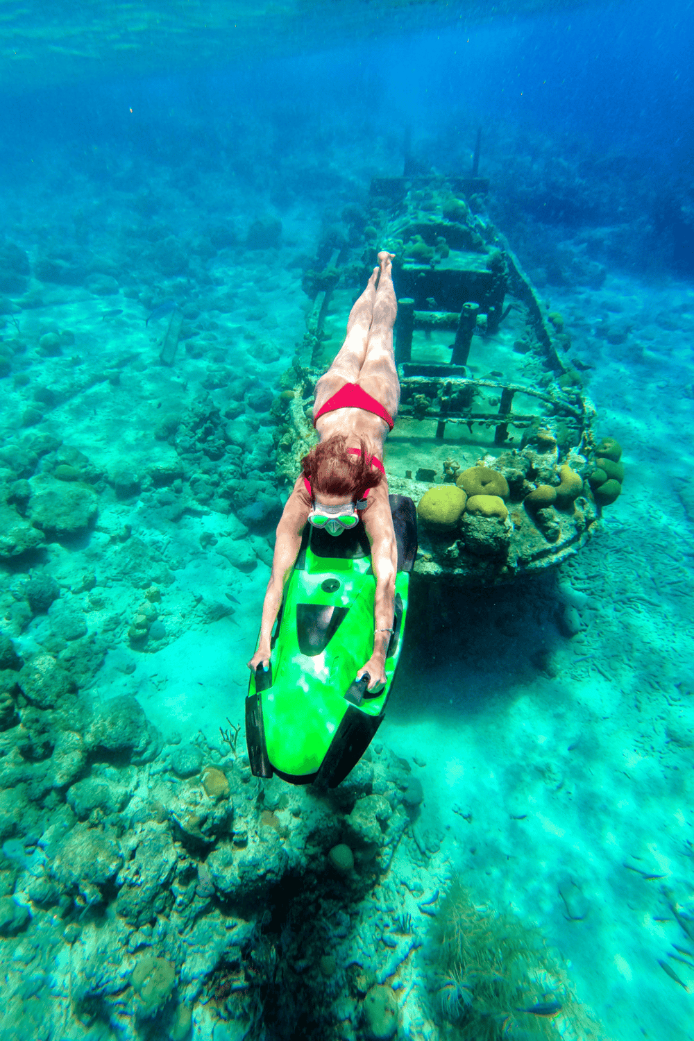 Underwater scuba diver gliding over sunken shipwreck in clear blue ocean waters.