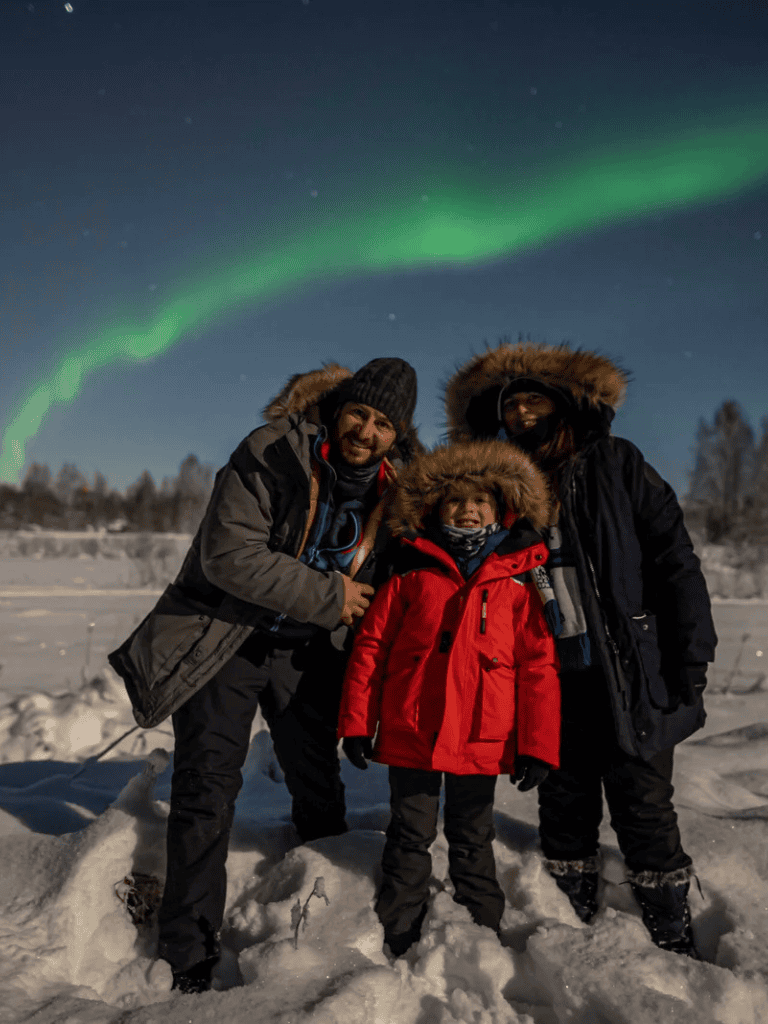 Aurora borealis over snowy landscape with family in winter gear, adventure, northern lights, travel, cold climate, outdoor activity.
