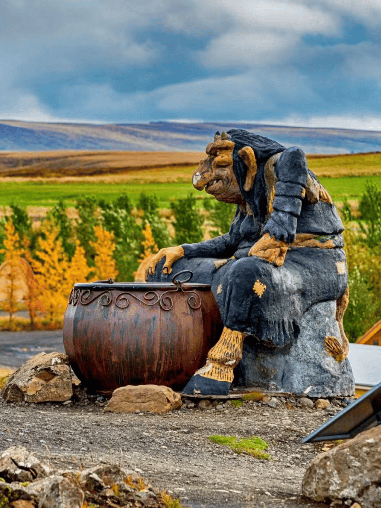 Carved stone troll sculpture in scenic mountain landscape with vibrant fall foliage.