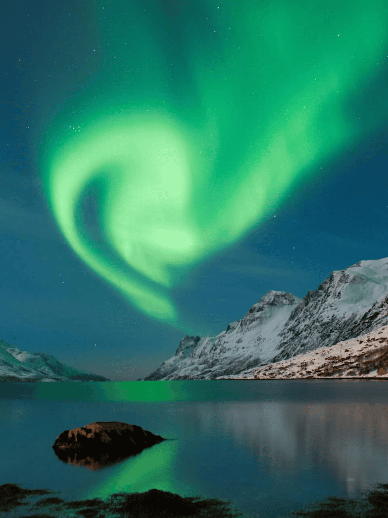 Northern Lights over Snowy Mountains and Lake at Night in Scandinavia.