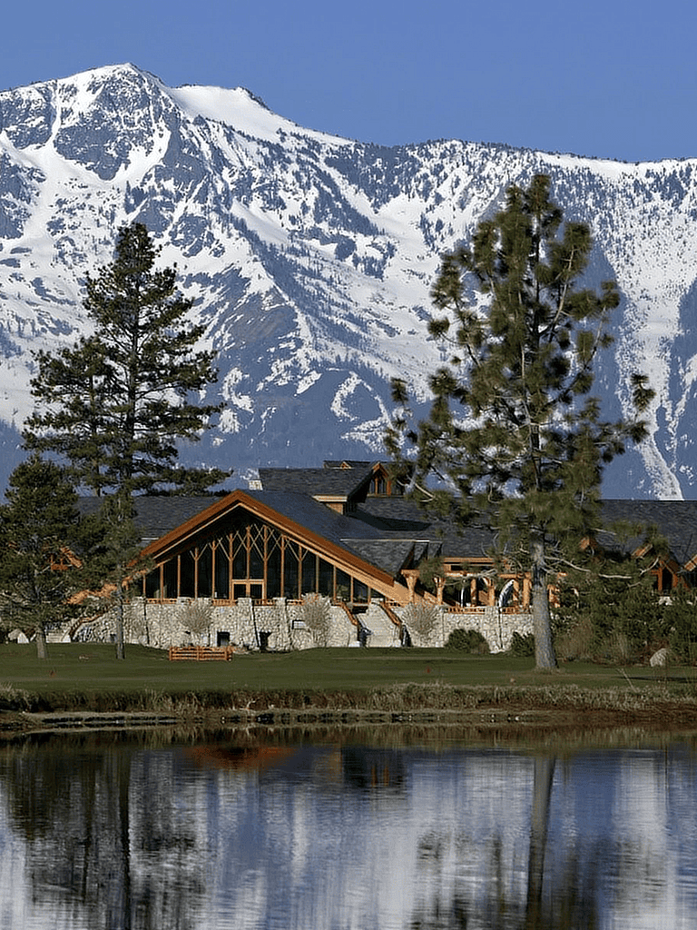 Snow-capped mountains with a lakeside lodge and pine trees, ideal for outdoor adventures and scenic retreats.