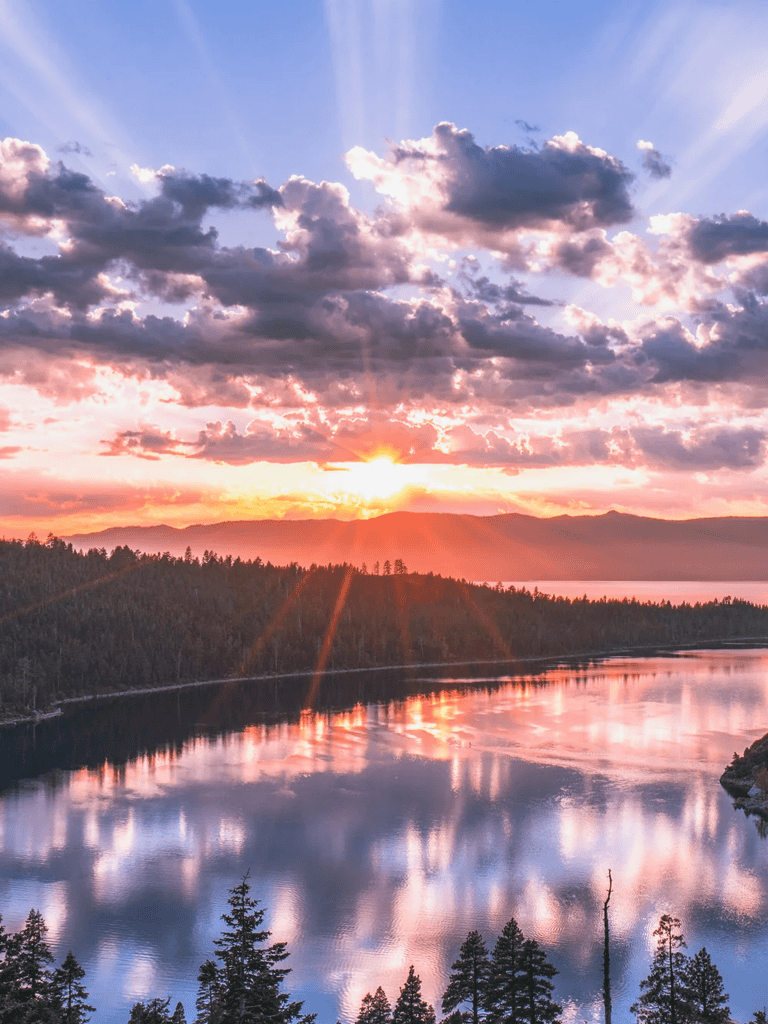 Breathtaking sunset over a tranquil river with mountains and pine trees, perfect for nature and travel enthusiasts.