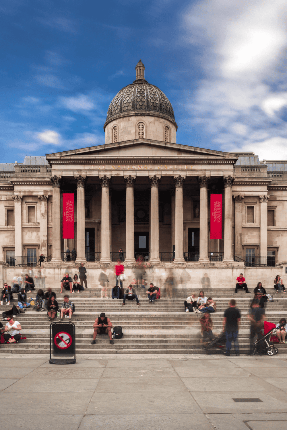 Historic National Gallery of Art in London with visitors on the steps under a blue sky.