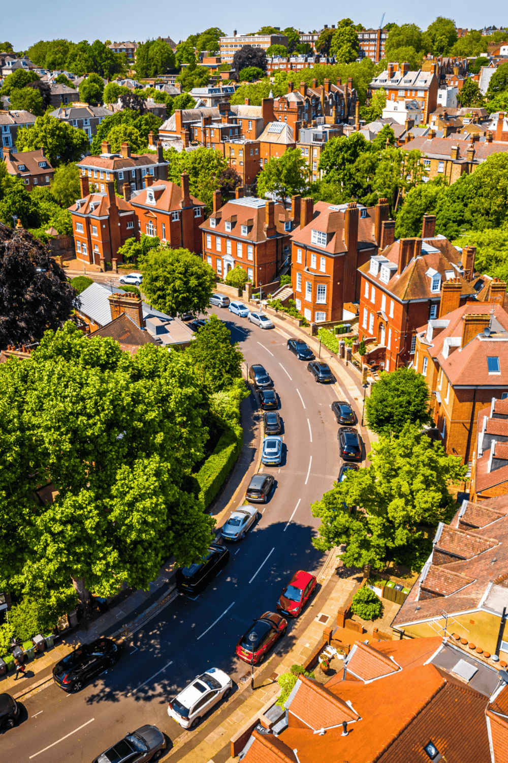 Aerial view of residential neighborhood with red brick houses surrounded by lush green trees.