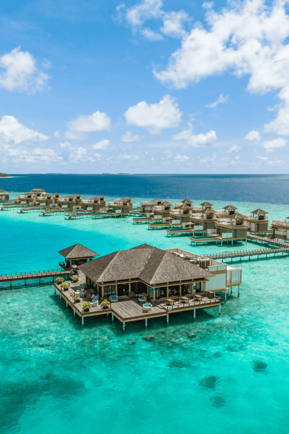 Overwater bungalow resort at tropical island paradise with turquoise waters and bright blue sky.